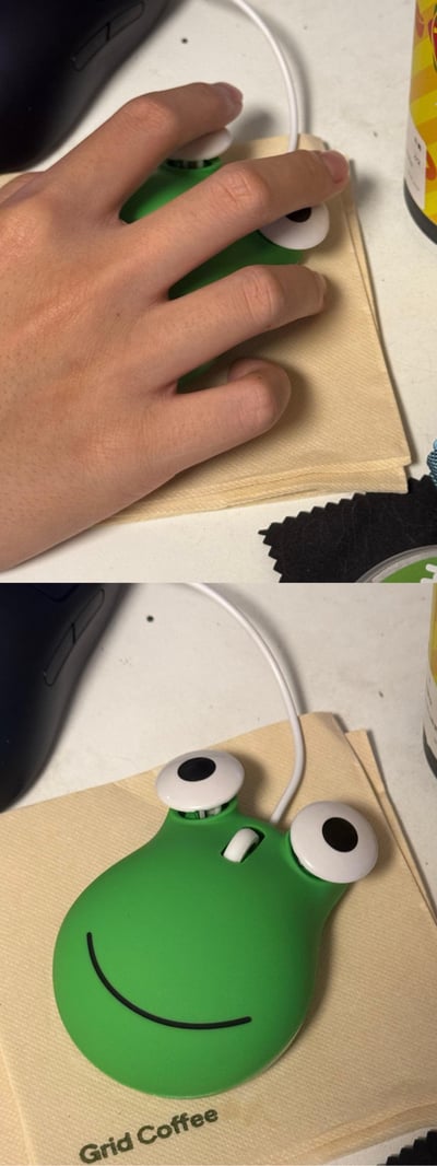 这是一组上下对比的实拍图，上图中一只手放置在绿色青蛙造型的有线鼠标上，两根手指恰好与鼠标的眼睛部件重合，制造出「手指是青蛙眼睛」的趣味视觉错位效果；下图展示了这款鼠标的真实样貌：绿色的鼠标本体带有黑色微笑线条，凸起的大眼睛造型十分可爱，鼠标被放在印有「Grid Coffee」字样的纸巾上，整体充满日常小趣味。