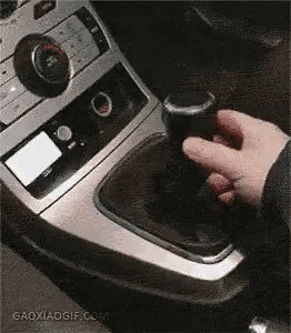 这是一段趣味动态实拍图，画面聚焦汽车中控台的换挡区域，一只手伸向看似是汽车换挡杆的物体，当手拿起后才发现这是一个外形高度模仿换挡杆的杯子，利用视觉错位制造出强烈的反差感，营造出迷惑又搞笑的效果，让人瞬间产生认知反差，充满整蛊趣味。