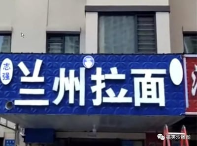 这是一张街边兰州拉面店铺的招牌实拍图，蓝色底搭配白色大字的招牌上，「兰州拉面」四个字因字体脱落出现趣味视觉错位：「兰」字的点脱落，恰好落在「拉」字的正上方，让「兰」字看起来像「三」，「拉」字则多了一笔，远看容易误看成「三州拉面」，制造出滑稽的视觉错觉。
这是由招牌字体脱落的巧合形成的无意搞笑梗，属于现实中出现的趣味视觉错位效果。