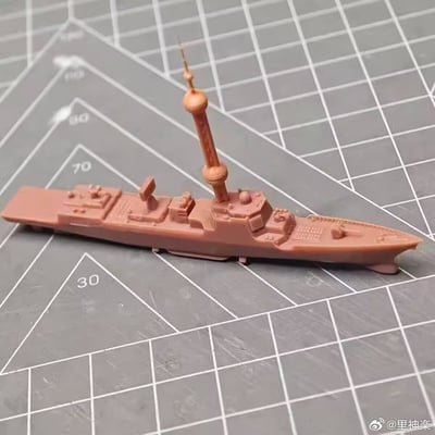 照片中展示了一艘粉色军舰模型，放置在带有白色网格线和数字刻度（30、70、80、90）的灰色切割垫上。模型细节丰富，包含高耸的桅杆、甲板设施、指挥塔等结构，整体呈现出未上色的原始塑料质感，可能处于制作或展示阶段。切割垫的网格背景清晰可见，为模型提供了规整的摆放环境，突出了模型的尺寸比例和精细做工。
