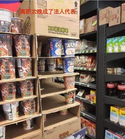 这是一张拍摄于超市的趣味梗图，画面展示了一个桶装泡面货架，货架上大部分位置已经空置，只剩下零星几桶泡面零散地留在货架上。图片上方添加了醒目的红色文字“离职太晚成了法人代表”，用超市里最后剩下无人选购的泡面，类比职场中最后离职的员工，调侃这类人往往会被迫留下承担额外的责任，如同“法人代表”一样要扛下后续的事务，用生活化的场景映射打工人的无奈与心酸，充满自嘲的幽默感。