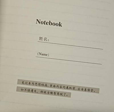 这是一张笔记本内页的照片，页面顶部印有英文“Notebook”字样，下方设有“姓名：”及对应英文“(Name)”的空白填写栏。最底部有两行手写风格的中文文字，内容为“笔记本为思想结晶，里面内容均属机密，应妥善保管。如不慎遗失，那就当缴智商税了。”。整体风格在正式的“机密保管”提醒后突然转折为幽默调侃，用网络流行语“智商税”制造反差笑点，展现了轻松诙谐的生活态度。
