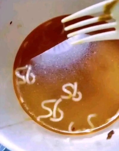 一张俯拍的食物照片，展示了一个白色碗中装着棕色的汤或 broth，里面有少量白色面条状物体，一只白色塑料叉子部分浸在汤中。