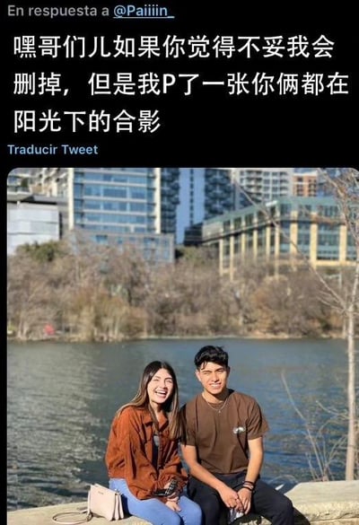 这是一张推特平台的社交媒体截图，画面上方是发布者的推文内容：“嘿哥们儿如果你觉得不妥我会删掉，但是我P了一张你俩都在阳光下的合影”，还标注了回复对象@Paiiiin_，以及“翻译推文”的西班牙文提示；画面下方是发布者P好的照片，照片里一男一女并肩坐在水边的石台上，背景是城市高楼与河流，两人都面带笑容，氛围温馨愉快。发布者提前告知对方若不满意可删除，尽显贴心，是网友间温暖的互动内容，图中没有双关、谐音梗等特殊内容。