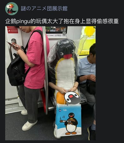 地铁场景中，一名乘客抱着一个巨大的企鹅Pingu玩偶，玩偶被透明塑料袋包裹着，体积庞大几乎遮住了乘客的上半身。旁边有其他乘客在看手机或休息，车厢内有广告和安全提示标识。图片上方配有文字“企鹅pingu的玩偶太大了抱在身上显得偷感很重”，幽默地调侃这么大的玩偶抱在身上容易让人产生误解，好像偷来的一样。