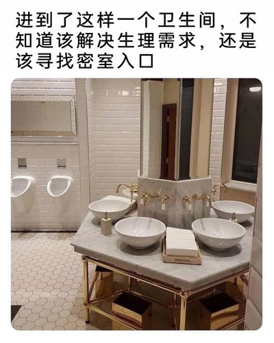 这是一张公共卫生间的实拍图，卫生间内的洗手台区域采用了多角镜面与大理石台面结合的设计，搭配四个台上式洗手盆，后方的镜面反射出旁边的小便池区域，形成了奇妙的视觉错位，让整个空间看起来像是存在一个类似密室入口的区域。图片上方配文调侃这种奇特的设计，让人分不清是要正常使用卫生间，还是要寻找密室入口。卫生间墙面是白色长条形瓷砖，地面是六边形瓷砖，整体装修风格偏精致，但特殊的布局带来了强烈的视觉错觉，充满趣味。