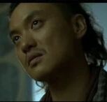图片中是一位扎着发髻的男性角色，身着深色传统服饰，面部表情严肃，眼神坚定地望向斜上方。背景色调较暗，整体氛围庄重，可能展现角色在思考或面对重要情境的状态。