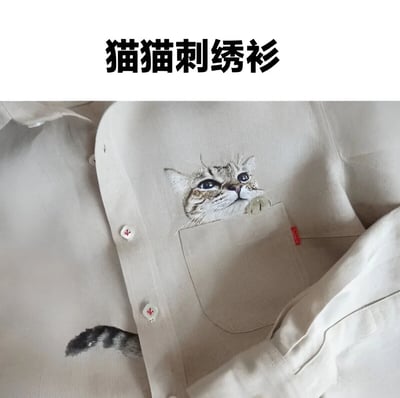 图片展示了一件米色的衬衫，核心亮点是胸前口袋处的精美猫咪刺绣图案：一只狸花猫的脑袋从口袋里探出，眼睛圆睁向上看，前爪搭在口袋边缘，神态灵动逼真；衬衫侧边还绣有一条猫尾巴作为呼应。图片顶部配有黑色加粗文字“猫猫刺绣衫”，整体构图清晰，突出了服饰的可爱设计感，属于典型的商品展示类图像。