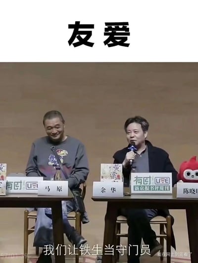 这是一张截取于文学对谈活动的趣味梗图，顶部标注了“友爱”二字，画面中作家马原和余华坐在活动现场的桌前，桌上摆放着他们的作品、姓名名牌以及“有时LIFE 新京报书评周刊”的标识。余华手持话筒正在发言，说出“我们让铁生当守门员”的话语，这里的“铁生”是指已故作家史铁生，因史铁生双腿不便，这个安排充满了老友间的调侃趣味，一旁的马原听到后露出笑容，整个画面展现出文坛老友间轻松诙谐的相处氛围。