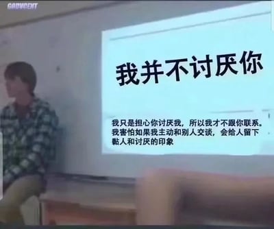 这是一张视频截图类的屏幕截图，属于图文混排的画面。画面左侧有一位穿着蓝白格子衬衫、卡其色裤子的人，他坐在讲台边缘，双手交握放在腿上，神情低落，看向画面一侧，神态显得局促不安。画面右侧的投影屏幕上是图文内容，最上方是醒目的大字“我并不讨厌你”，下方配有小字解释：“我只是担心你讨厌我，所以我才不跟你联系。我害怕如果我主动和别人交谈，会给人留下黏人和讨厌的印象”。这段文字精准地传达出社恐人群在人际交往中的矛盾心理：本身并不排斥他人，却因为过度担忧自己的主动会给对方带来困扰、留下不好的印象，从而选择回避社交，独自承受内心的不安，很容易引发有类似心理状态人群的共鸣。