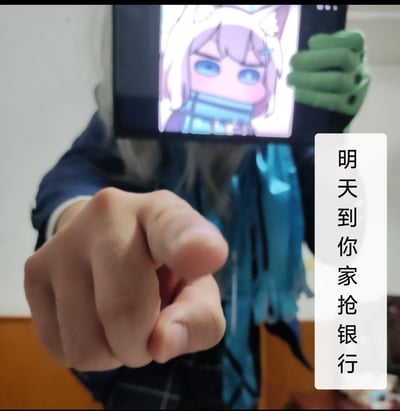 这是一张网友自制的趣味合成梗图：将显示着《蔚蓝档案》角色砂狼白子Q版生气脸的手机放在真人头部位置，真人伸出手指指向镜头，图片右侧加注文字‘明天到你家抢银行’。用可爱的动漫生气脸和夸张的放话语句形成反差感，制造出滑稽搞怪的效果，没有双关、谐音梗或暗示内容，纯为整活搞笑。