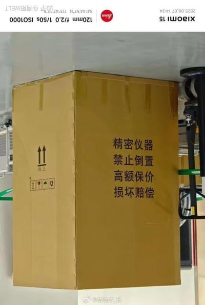 图片中展示了一个黄色的纸箱，放置在室内角落。纸箱表面印有黑色文字：'精密仪器 禁止倒置 高额保价 损坏赔偿'，左侧有向上箭头标识及多个搬运提示图标。箱子整体呈立方体，背景可见部分室内设备，可能是在仓库或快递分拣区域。图片通过突出纸箱上的警示文字，暗示物品的贵重性及对正确搬运的严格要求。