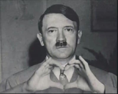这是一张经过P图改编的黑白历史人物照片，图中人物的鼻子被替换成了类似小胡子的装饰，同时双手做出比心的手势。原本严肃的人物形象与温情搞笑的比心动作形成强烈反差，制造出恶搞的喜剧效果。