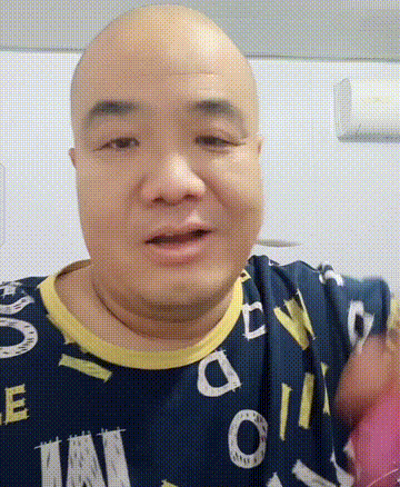 这是一段真人动态GIF，画面主体是一位光头中年男性，他身着带有白色、黄色字母图案的深色上衣，身处简单的室内环境中。该男性面部呈现出惊讶又略带激动的神情，同时手部做出比划的动作，身体有轻微晃动，整体情绪外放，适合用来表达诧异、激动的心情。