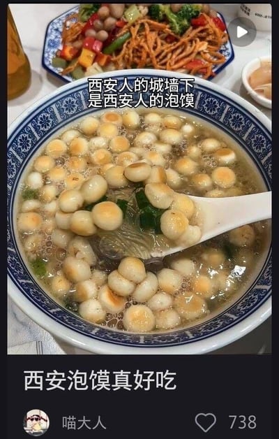 图片主体是一碗西安泡馍，盛在蓝白花纹的瓷碗中，汤里漂浮着许多小巧的面团，汤面泛着油花，还点缀着绿色的葱花，一把白色勺子正从碗中舀起部分泡馍。背景中可见一盘色彩丰富的炒蔬菜，包含西兰花、红椒、黄椒和虫草花等食材。图片上方有文字“西安人的城墙下是西安人的泡馍”，下方有文字“西安泡馍真好吃”，整体呈现出诱人的美食场景，突出西安特色小吃泡馍的美味。
