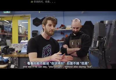 这是一张科技自媒体Linus Tech Tips的视频截图，画面呈现充满工具和设备的工作室场景，左侧是主持人Linus Sebastian，他摊开双手，表情略带戏谑，似乎在发起一项趣味挑战；右侧是一位工作室成员，双臂交叉抱胸，低头露出似笑非笑的神情。画面顶部有弹幕“你说的对，但是。。。”，下方配有中英双语字幕，中文内容为“看看他能不能说'你说得对'后面不接'但是'”。这个内容调侃了日常沟通中常见的现象：人们在说出“你说得对”之后，往往会用“但是”来转折，表达不同的观点，这个挑战正是要打破这个惯性沟通方式，充满轻松戏谑的趣味。