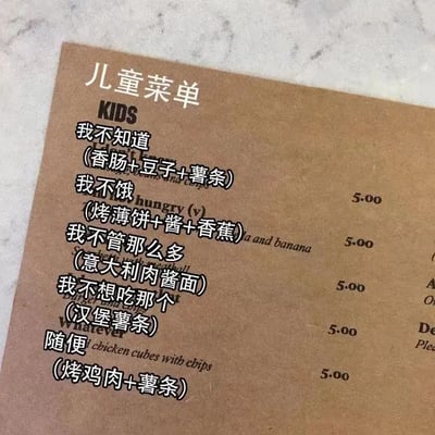 这是一张加注了中文的儿童菜单实拍图，原本的英文菜单设计十分有创意，将小朋友被家长询问想吃什么时最常给出的模糊答复直接作为菜品名称，每款名称后标注了对应的实际餐食内容，售价统一为5。中文标注精准还原了家长给孩子点餐时频繁收到这类答复的日常场景，充满幽默感，很容易引发家长群体的共鸣。