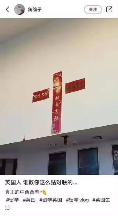 这是一张社交媒体平台的截图，内容核心是英国一处建筑外墙上的特殊春联张贴方式：当地人将中国传统的竖版春联作为竖杆，两个横版横批分别贴在竖联的上下两端，组合成了西方基督教十字架的视觉造型。竖联文字为“财气吉祥”，两个横联为常见的新春祝福类文字。截图的配文部分，发布者吐槽“英国人 谁教你这么贴对联的...”，并调侃这是“真正的中西合璧”，搭配了哭笑不得的表情。该内容是留英学生分享的当地生活日常，通过中国春节习俗与西方宗教符号的错位结合，制造出荒诞搞笑的效果，引发网友对文化碰撞趣事的关注。