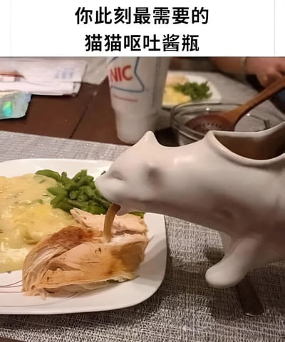 图片展示了一个白色陶瓷猫猫形状的酱瓶，正将酱汁倾倒在一盘食物上（包含鸡肉、青豆和奶油状食物）。猫猫酱瓶的倾倒姿势因造型设计看起来酷似呕吐动作，形成荒诞又搞笑的视觉效果。图片顶部有黑色加粗文字“你此刻最需要的猫猫呕吐酱瓶”，强化了幽默氛围。