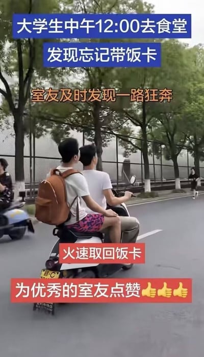 这是一张标注了文字的校园实拍静态图，画面主体为两名男大学生同乘一辆白色电动车行驶在校园道路上，路旁排列着行道树和围栏，远处还能看到其他行人和行驶的电动车。图上叠加了多段说明文字：顶部蓝色背景文字介绍背景为大学生中午12点去食堂时发现忘记带饭卡，中间橙色文字说明室友及时发现后一路狂奔，中部偏下红色文字标注两人火速取回饭卡，最底部红色背景文字配三个点赞表情，表达对热心室友的称赞，整体展现了大学校园里室友之间互助的暖心日常。
