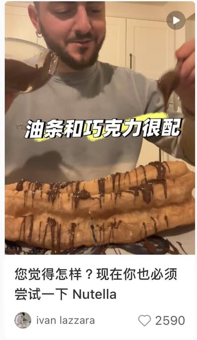 这是一张海外社交平台的用户原创内容截图，画面主体是一位留着胡子的外国男士，正手持容器和勺子往两根超大的中式油条上淋Nutella（能多益）榛子巧克力酱，油条表面已经覆盖了不少流淌的巧克力酱。图中配有醒目的中文文字“油条和巧克力很配”，下方的配文则以中文结合英文的方式写道“您觉得怎样？现在你也必须尝试一下Nutella”。这条内容的发布者账号为ivan lazzara，获得了2590个点赞，是将中式传统早餐与西式流行酱料结合的新奇美食搭配，旨在向网友推荐这种独特的吃法。