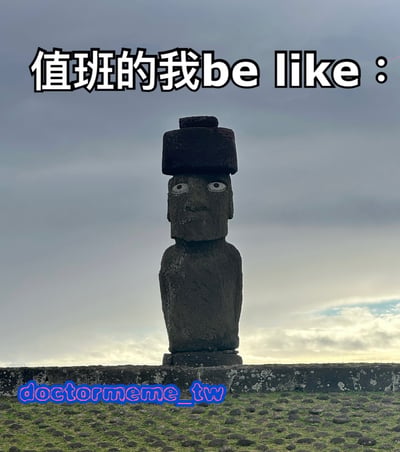 图片主体为复活节岛的摩艾石像，石像头部巨大，戴着圆柱形石帽，面部表情呆滞，双眼圆睁，背景是阴沉的多云天空。图片顶部有醒目的文字“值班的我be like：”，通过将值班时的状态与摩艾石像的僵硬、呆滞形象进行类比，幽默地表达了值班时的无聊、困倦和机械感，充满了职场打工人的共鸣感。