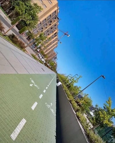这是一张利用特殊拍摄角度打造的创意城市街景照片。画面中的绿色自行车道，因拍摄视角的倾斜，与旁边的人行道、建筑形成了强烈的视觉错觉，看起来仿佛是垂直向下的悬崖边缘，给人一种骑行者即将驶入深渊的奇妙视觉冲击，充满趣味与创意。