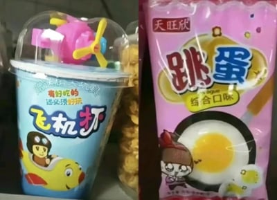 这是一张左右对比的静态图，展示了两款存在低俗擦边球命名问题的儿童零食：左侧是蓝色杯装的“飞机杯”零食，杯身印有卡通飞行员坐在拟人化黄色飞机上的图案，杯盖附带粉色飞机造型玩具，杯身标注宣传语“赠送精美玩具 有好吃的 还必须好玩”；右侧是粉色包装的“天旺欣”牌“跳蛋”综合口味零食，包装印有表情无奈的卡通女孩和煎蛋图案。两款零食的名称均与成人用品同名，利用双关、谐音的低俗擦边球方式命名，容易让消费者产生不当联想，可能对儿童造成不良引导。