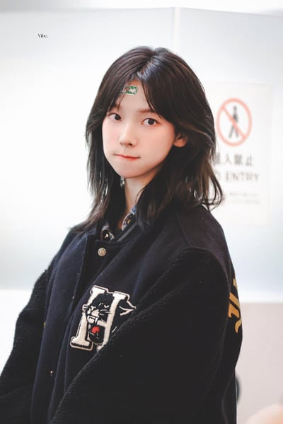 这是一张艺人李紫婷的饭拍路透照片，她留着深色中长发，额头贴着一块带图案的创可贴，身穿带有黑豹刺绣图案的深色棒球服，表情软萌地看向镜头，背景是带有“禁止进入”标识的室内场所，整体风格清新乖巧，给人一种邻家感十足的氛围。