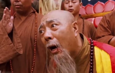 这是古装喜剧《乌龙闯情关》的经典截图，画面核心是寺庙方丈，他双眼瞪大向上凝视，嘴巴大张，胡须和嘴角带有血迹，面露极度惊恐的神情，身体前倾；身后的其他僧人穿着僧袍，表情各异，有的双手合十，整体场景传递出强烈的意外与震惊感，该画面常被制作成表情包，用于表达不敢置信、极度错愕的情绪。