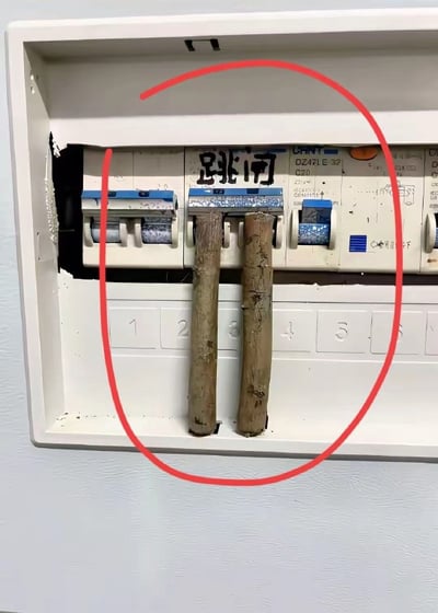 图片展示了一个白色的家用配电箱内部，中间编号为3的断路器位置被两根粗糙的木棍垂直插入，强行将可能跳闸的断路器卡住。断路器上方用黑色马克笔手写“跳闸”二字，整个违规操作区域被红色圆圈醒目标注。这种行为严重违反电气安全规范，可能导致电路过载无法自动断电，存在极大的火灾和触电风险。