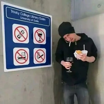 图片左侧是都柏林圣三一学院图书馆的蓝色禁止标识牌，上面用英文写着“Trinity College Library Dublin University of Dublin”，并配有四个禁止图标：禁止使用手机（带斜线的手机图案）、禁止饮酒（带斜线的酒杯图案）、禁止进食汉堡（带斜线的汉堡图案）、禁止吸烟（带斜线的香烟图案）。标识牌右侧站着一名身穿黑色连帽衫和黑色帽子的男子，他左手拿着一杯红酒，右手拿着一个汉堡，正在用手机打电话，嘴里还叼着一根香烟，完美违反了标识牌上的所有禁止规定，形成强烈的幽默对比。