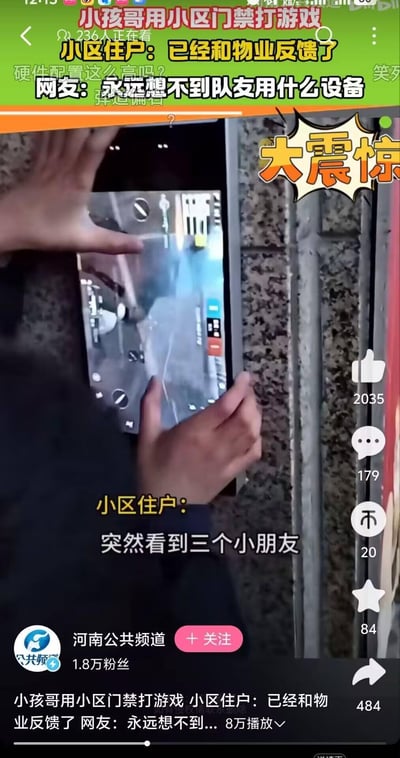 这是一段B站平台的视频截图，画面里一名小孩正操作小区的门禁显示屏玩射击类游戏，双手在屏幕上进行操作，屏幕清晰显示着射击游戏的画面。画面上方配有醒目标题文字：“小孩哥用小区门禁打游戏 236人正在看 小区住户：已经和物业反馈了 网友：永远想不到队友用什么设备”，右侧还有“大震惊”的趣味贴纸；画面下方字幕是小区住户的描述：“突然看到三个小朋友”。视频界面显示该内容由河南公共频道发布，拥有1.8万粉丝，视频播放量8万，点赞2035、评论179、收藏84、转发484。整体内容充满趣味性，网友调侃游戏队友的操作设备千奇百怪，小区住户已向物业反馈小孩使用门禁设备打游戏的情况。