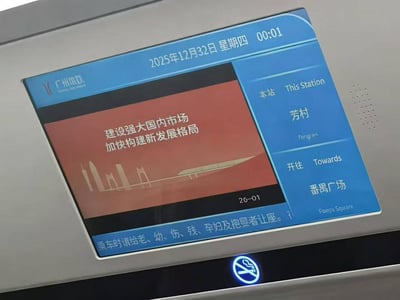 广州城际列车车厢内的电子显示屏截图，屏幕顶部显示错误日期“2025年12月32日 星期四 00:01”（12月实际仅31天），引发网友调侃“32号发车”。屏幕左侧为红色背景的宣传标语“建设强大国内市场 加快构建新发展格局”及城市天际线剪影，右侧标注当前站“芳村”（Fangcun）、开往“番禺广场”（Panyu Square），底部有“乘车时请给老、幼、伤、残、孕妇及抱婴者让座”的提示文字，右下角配有禁止吸烟标识。