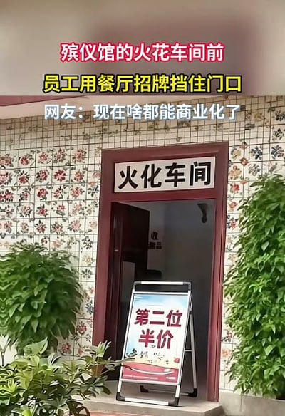 这张图展示了殡仪馆的场景，画面主体是写有“火化车间”字样的门口，门口放置了一个促销广告牌，广告牌上标注“第二位半价”；图上方叠加了三段说明文字，红色文字为“殡仪馆的火花车间前”（应为笔误，实际指代火化车间），黄色文字为“员工用餐厅招牌挡住门口”，白色文字为“网友：现在啥都能商业化了”。门口两侧布置有绿植，背景是带花卉图案的瓷砖墙面，促销标语和火化车间的场景形成强烈反差，产生了黑色幽默的效果。